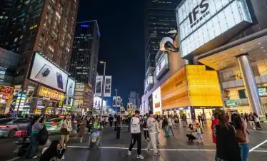 Vibrant city street scene at night with illuminated billboards, busy pedestrians, and high-rise buildings showcasing luxury brands and popular stores, capturing the energetic urban nightlife.